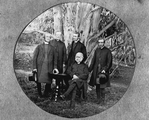 A group of ministers in front of a tree, one seated and the rest standing.