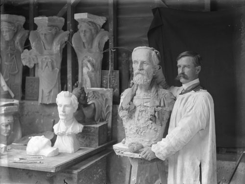 A photograph of Charles Kidson posing with a carved bust and other items of sculpture
