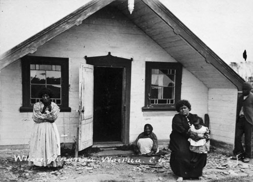 Kiti Karaka Rīwai (seated with child, right) in front of the meeting house she helped build at Wairua, Chatham Island, in the 1890s
