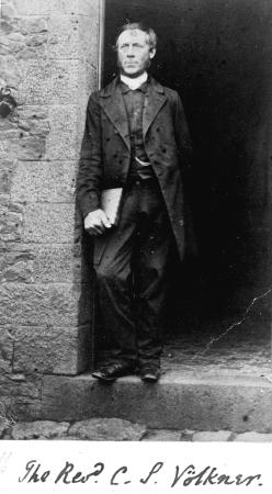 Carl Volkner standing in a doorway and wearing clerical garb