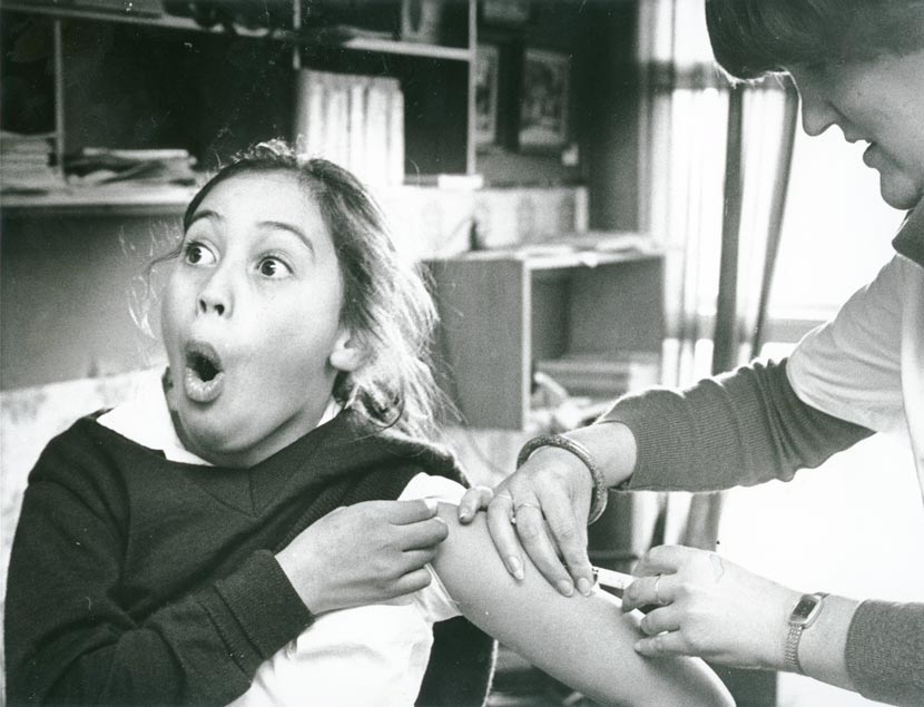 A young girl makes a surprised face as a woman injects her with a vaccine.