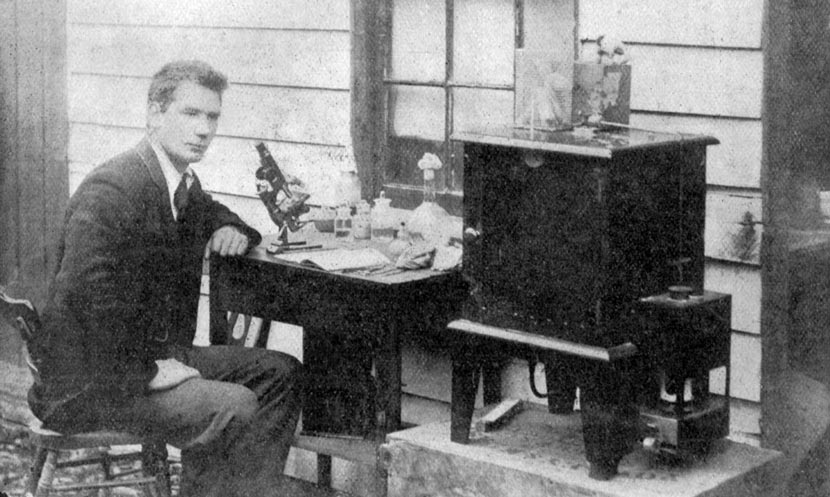 A man sitting at a desk with a microscope and other scientific equipment.