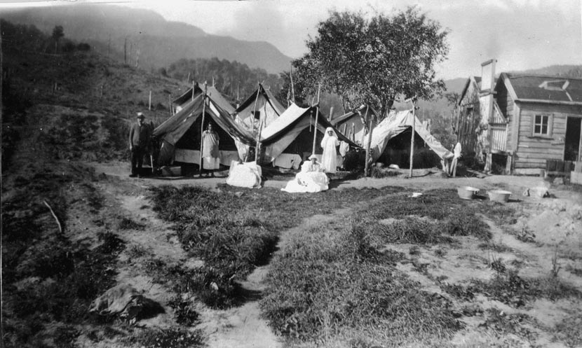 Nurses and others stand in front of tents next to a simple wooden house in a remote area.