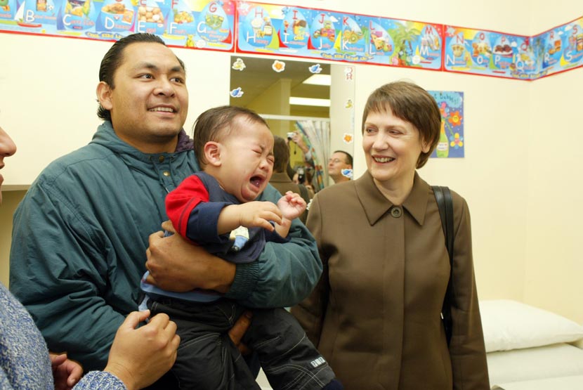 A man holding a crying child standing next to a woman.