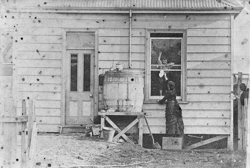 A run-down house with a child at a window with a woman reaching up to him.