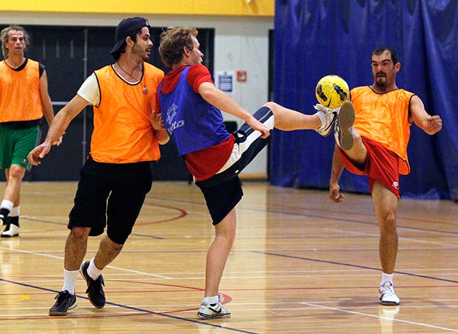 Men wearing coloured bibs competing to kick a ball on a court.