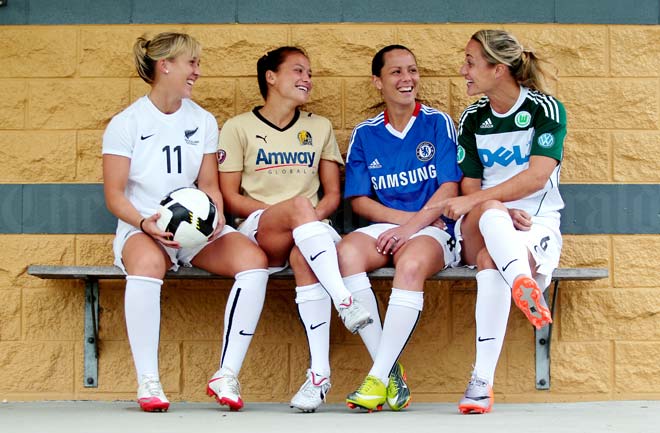 Four women sitting on a bench in various coloured sports uniforms laughing and smiling.