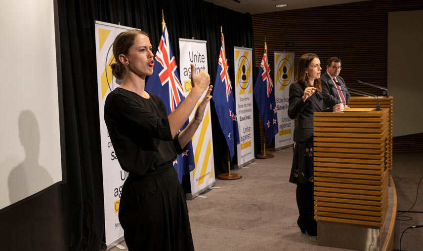 Woman signing in the foreground with PM and Minister Robertson at podium in background.