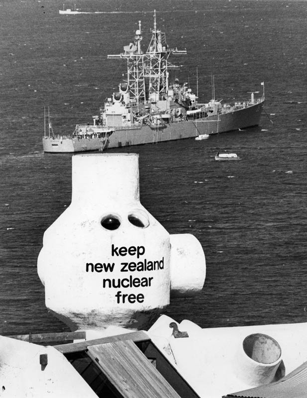 A photograph showing the look-out tower on the roof of Athfield’s house bearing the slogan ‘keep New Zealand nuclear free’, with an American warship in the harbour in the background