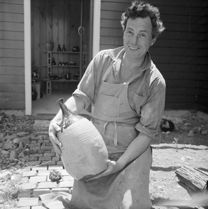 Jack Laird in middle age, standing outdoors in an apron and holding a large pot. 