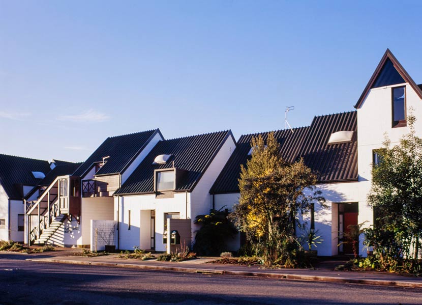 A collection of white townhouses with grey roofs of different sizes and shapes.