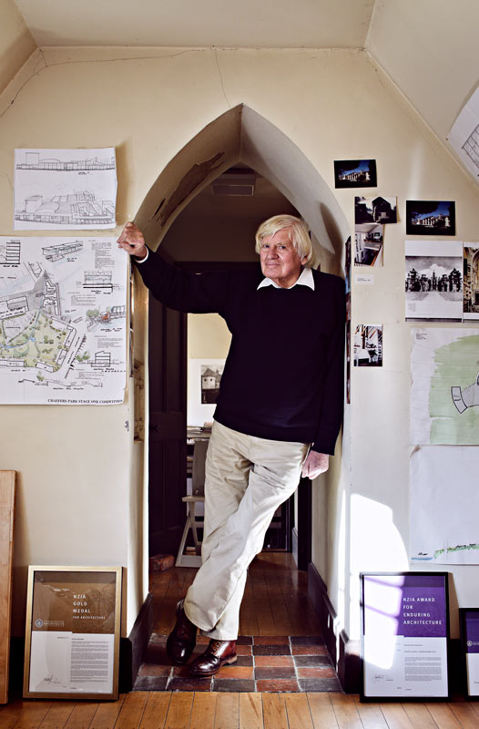 Peter Beaven standing in an arched doorway, surrounded by architectural drawings pinned on the wall.