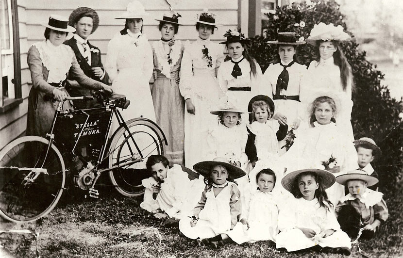 Black and white photograph of a man, women and children standing and sitting next to a motor bicycle with the words 'Stella' Temuka on it.