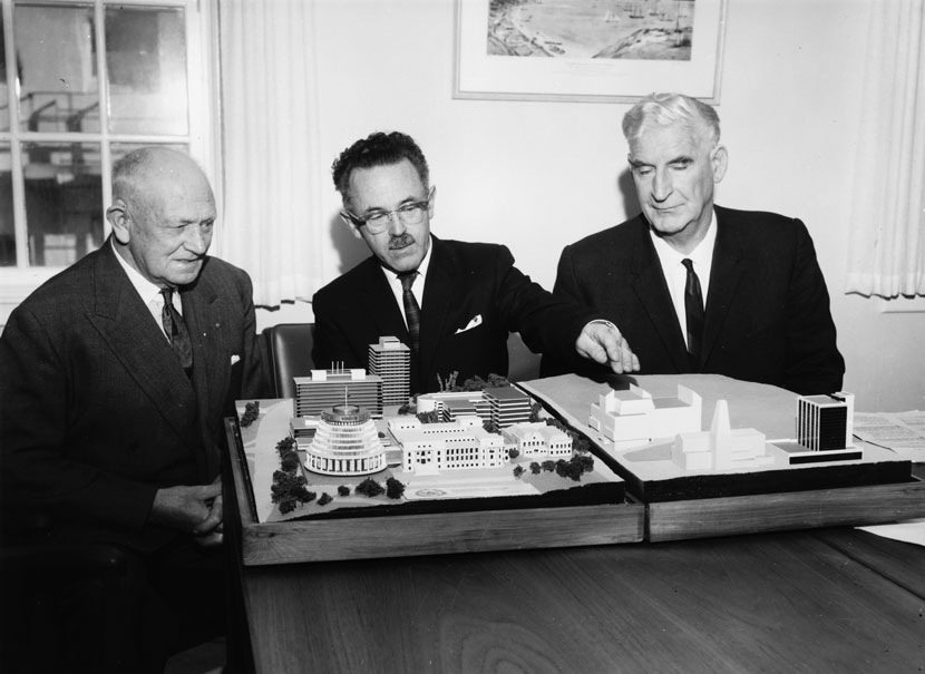 Three men sit behind an architectural model of buildings in the New Zealand parliamentary precinct in central Wellington.
