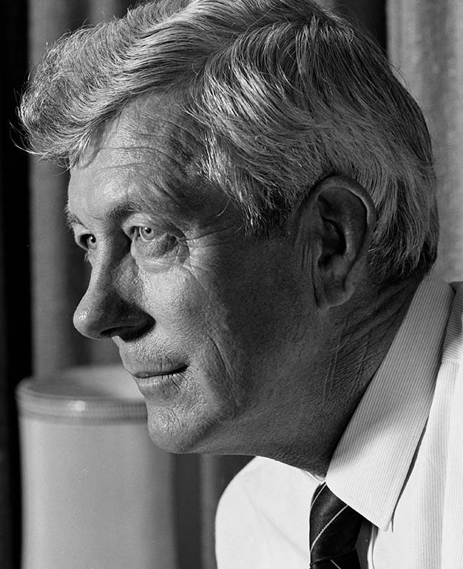 A black and white, head and shoulders portrait of Ian Cross in middle age, photographed in profile looking pensively off to the left. 