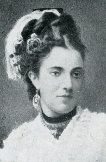 Black and white formal portrait of a young Anne Wilson wearing floral headwear and large earrings.