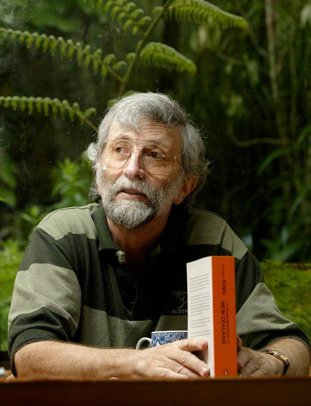 Michael King, seated at an outdoor table, holding a copy of his book.