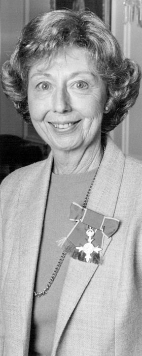 A photograph of a smiling Jean Wishart with an OBE medal pinned to her jacket.