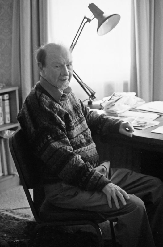 A photograph of Bill Pearson as an elderly man, seated beside a desk with a lamp and papers on it. 
