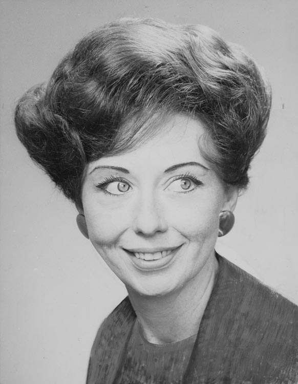 A glamorous head and shoulders studio portrait of Jean Wishart at 42, wearing make-up and large round earrings, with elegantly styled hair. 