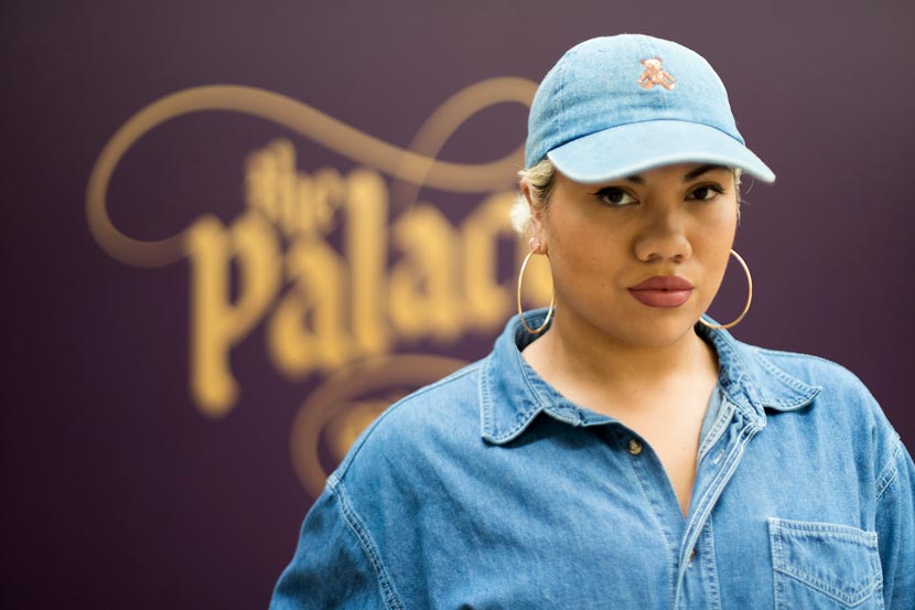 Head and shoulders view of Parris Goebel wearing gold hoop earrings, blue denim shirt and hat.