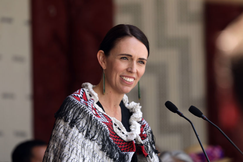 Smiling Jacinda Ardern standing at lectern wearing Māori cloak