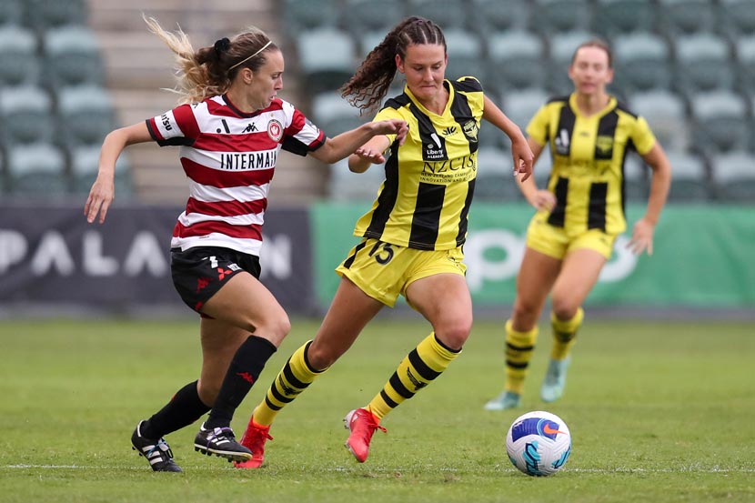 A women in a yellow uniform shown during a football game contesting the ball against a player in a striped red and white uniform. 