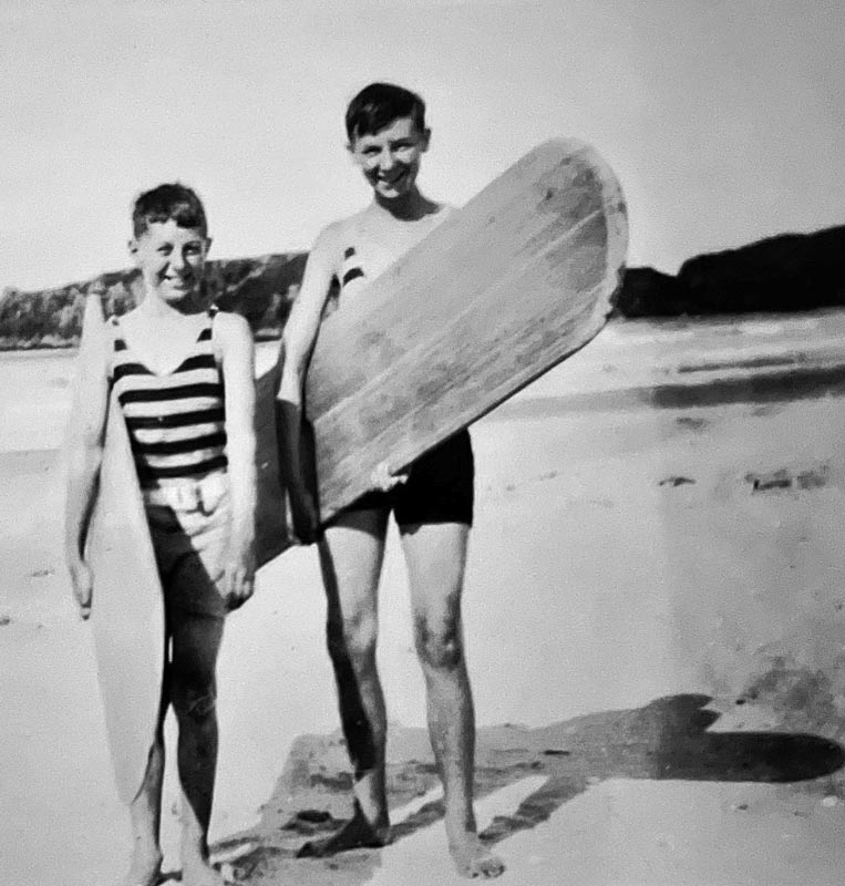 Two boys in swimsuits holding surfboards at a beach.