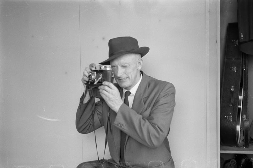 A man in a suit holds a camera to his face.
