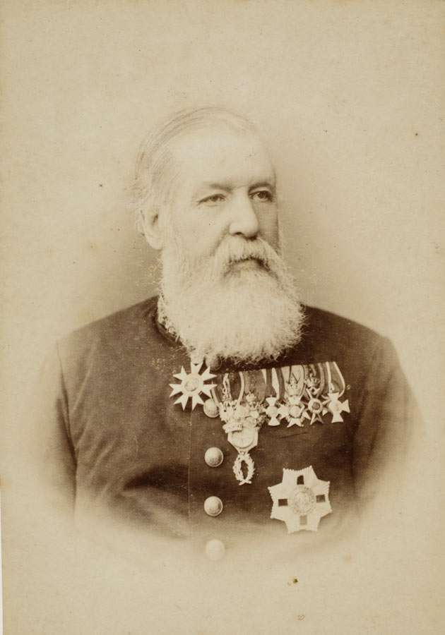 A studio portrait of a heavily bearded man in later life, with nine medals pinned to his breast.