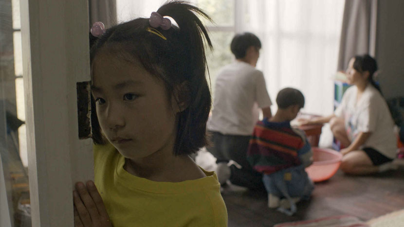 Young Asian girl leaning against a door with three people sitting on the floor in the background