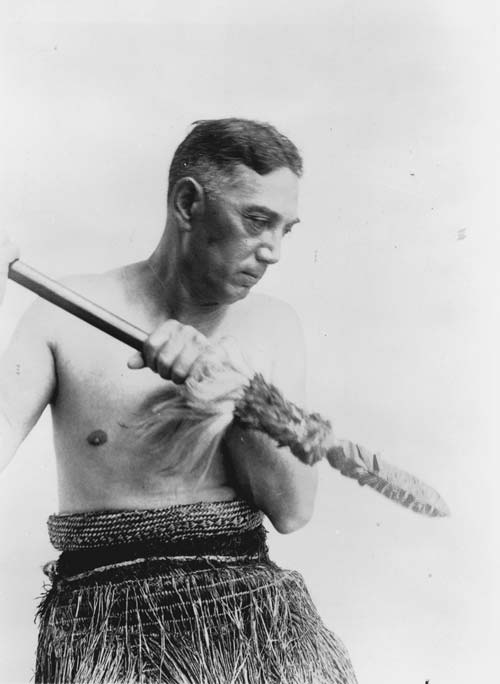 Peter Henry Buck in traditional Māori dress, holding a taiaha
