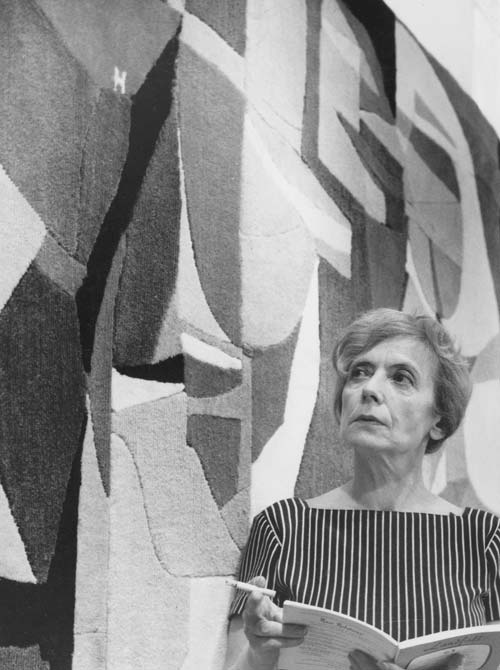 Photograph of Loiuse Henderson in front of a wool mural