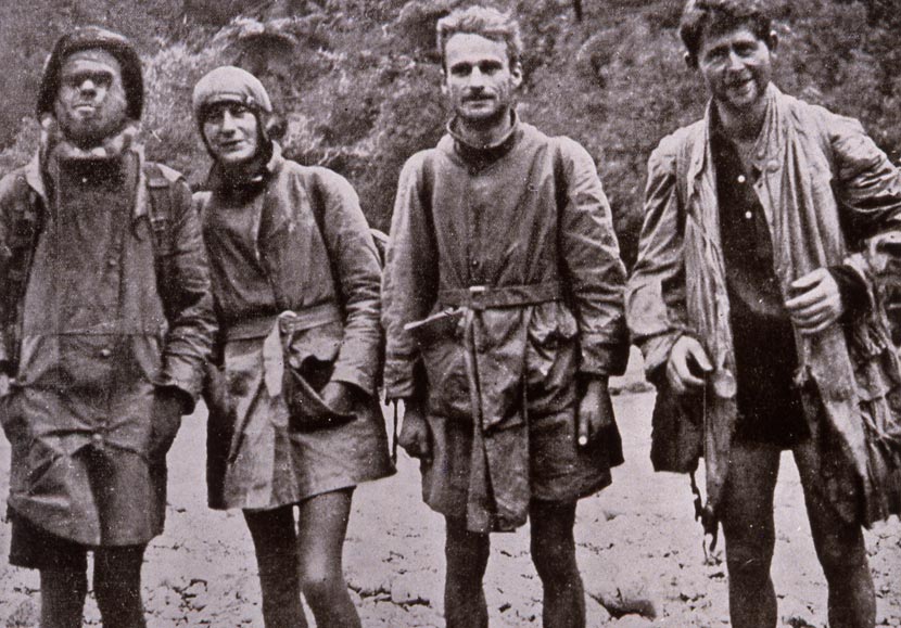 Three men and one woman wearing tramping gear standing on a river bed