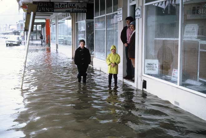 Children standing flood waters in front of a shop. 