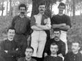 A group of ten male players standing and sitting together under a tree, many with moustaches, wearing uniforms that do not match