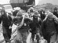 A large group of people in wet weather clothing set off up a muddy road with a truck behind them. 