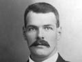 Man with moustache seated in suit and tie
