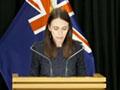 A woman speaking from a podium in front of three New Zealand flags, with a sign language interpreter at her side.