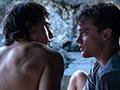 Two young men, one shirtless, staring into each other's eyes intimately.