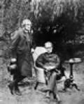 A photograph of two men under a tree, one standing and one seated