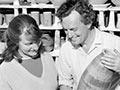 Peggy and Jack Laird in middle age, standing in the pottery workshop with a variety of completed pottery items. 