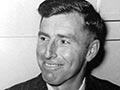 A black and white head and shoulders photograph of Roly Earp, smiling, wearing a suit and tie. 