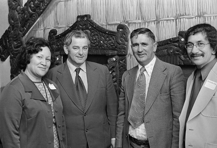Three men and a woman in front of Māori whare in Parliament.
