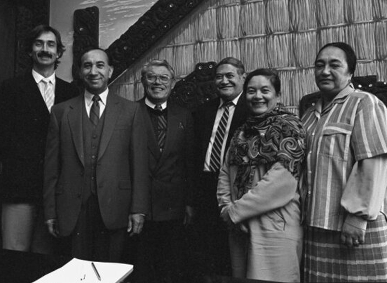 Four males and two females standing in from of a Māori meeting house in Parliament.