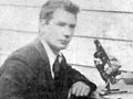 A man sitting at a desk with a microscope and other scientific equipment.