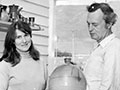 Peggy and Jack Laird, in middle age, standing in their shop with a variety of pots on shelves. 