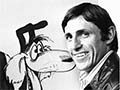 Murray Ball as a young man, seated beside an enlarged illustration of the Wal’ and Dog ‘Footrot Flats’ characters. 