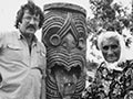 Michael King and Whina Cooper, standing either side of a carved pou (pole). 