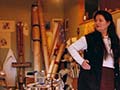 Pauline Thompson, in middle age, stands in a room cluttered with artworks, cardboard storage rolls, paints and other artists’ equipment. 